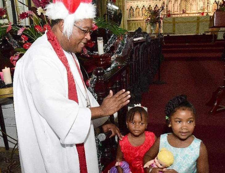 Holy Gifts: Fr Carl Williams blesses Malia Taylor, right, and Danae Norgrif with their Christmas gifts during yesterday’s Holy Innocents service at the Holy Trinity Cathedral, Port of Spain. —Photo: ISHMAEL SALANDY